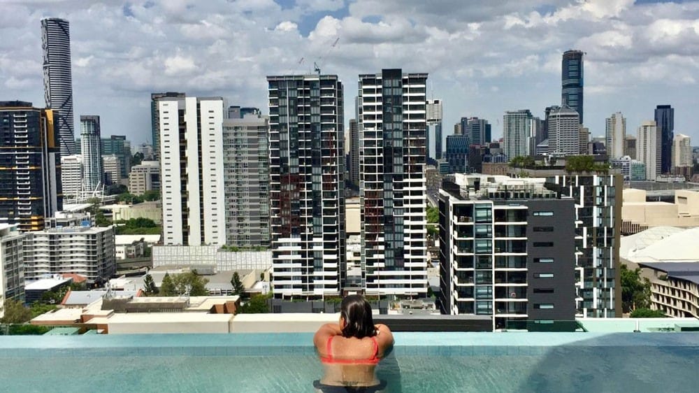 chica en bikini de espaldas y en una piscina y delante los edificios
